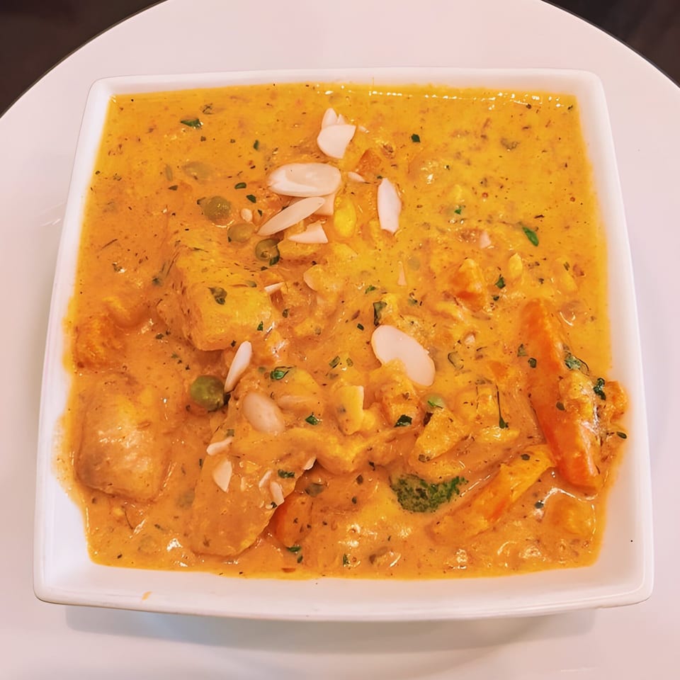 PIND Indian Cuisine's creamy orange curry with vegetables, paneer, and sliced almonds in a white square bowl.