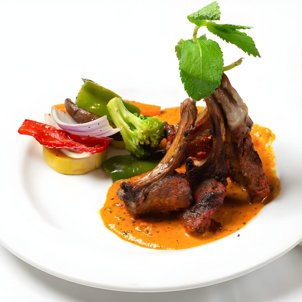 PIND Indian Cuisine's lamb chops with sauce, garnished with mint and a side of colorful vegetables.