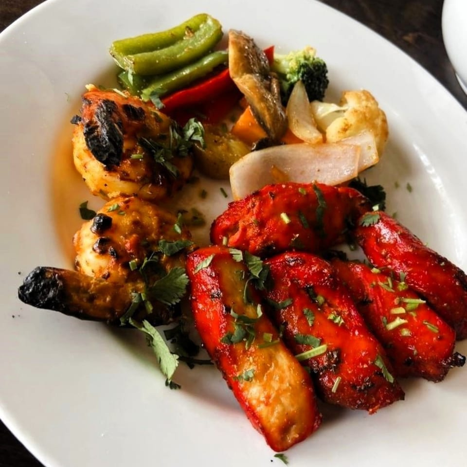 A white plate with PIND Indian Cuisine's grilled chicken, shrimp, and mixed vegetables.