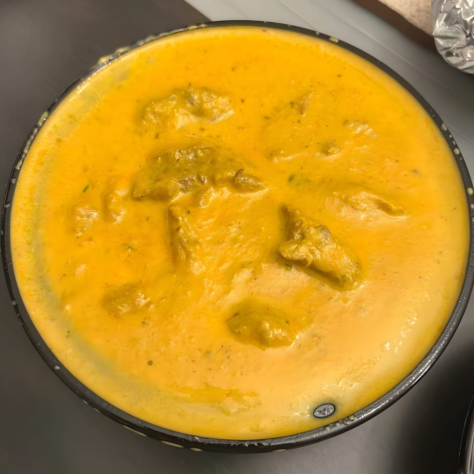 A close-up, overhead view of a vibrant orange Indian curry dish with chicken pieces in a black bowl.